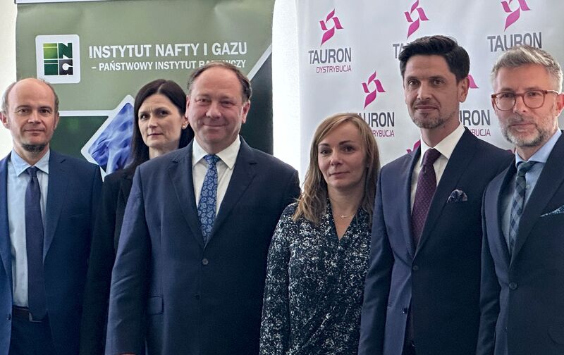 czterech panów i dwie panie stoją na tle banerów Instytutu Nafty i Gazu oraz TAURON Dystrybucji
