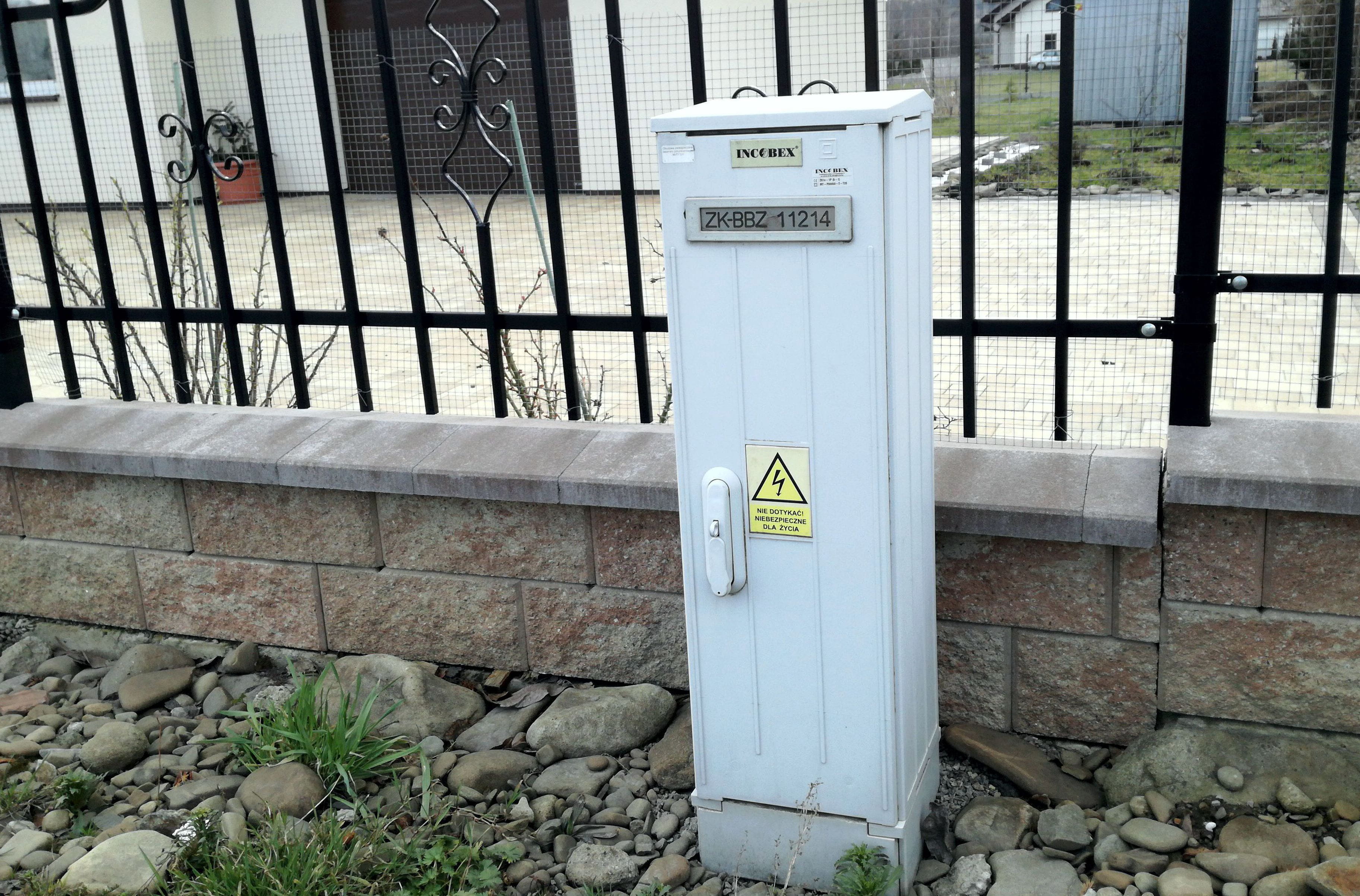 szafka energetyczna złącza kablowego stojąca przed płotem nowego domu jednorodzinnego