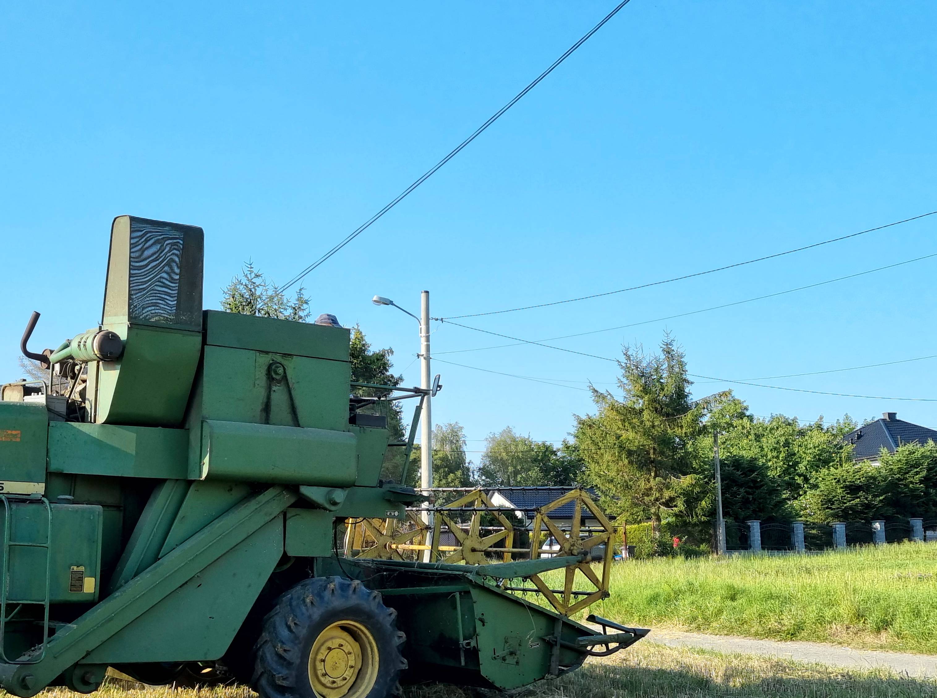 kombajn stoi w bliskiej odległości od zwisającego przewodu z linii energetycznej