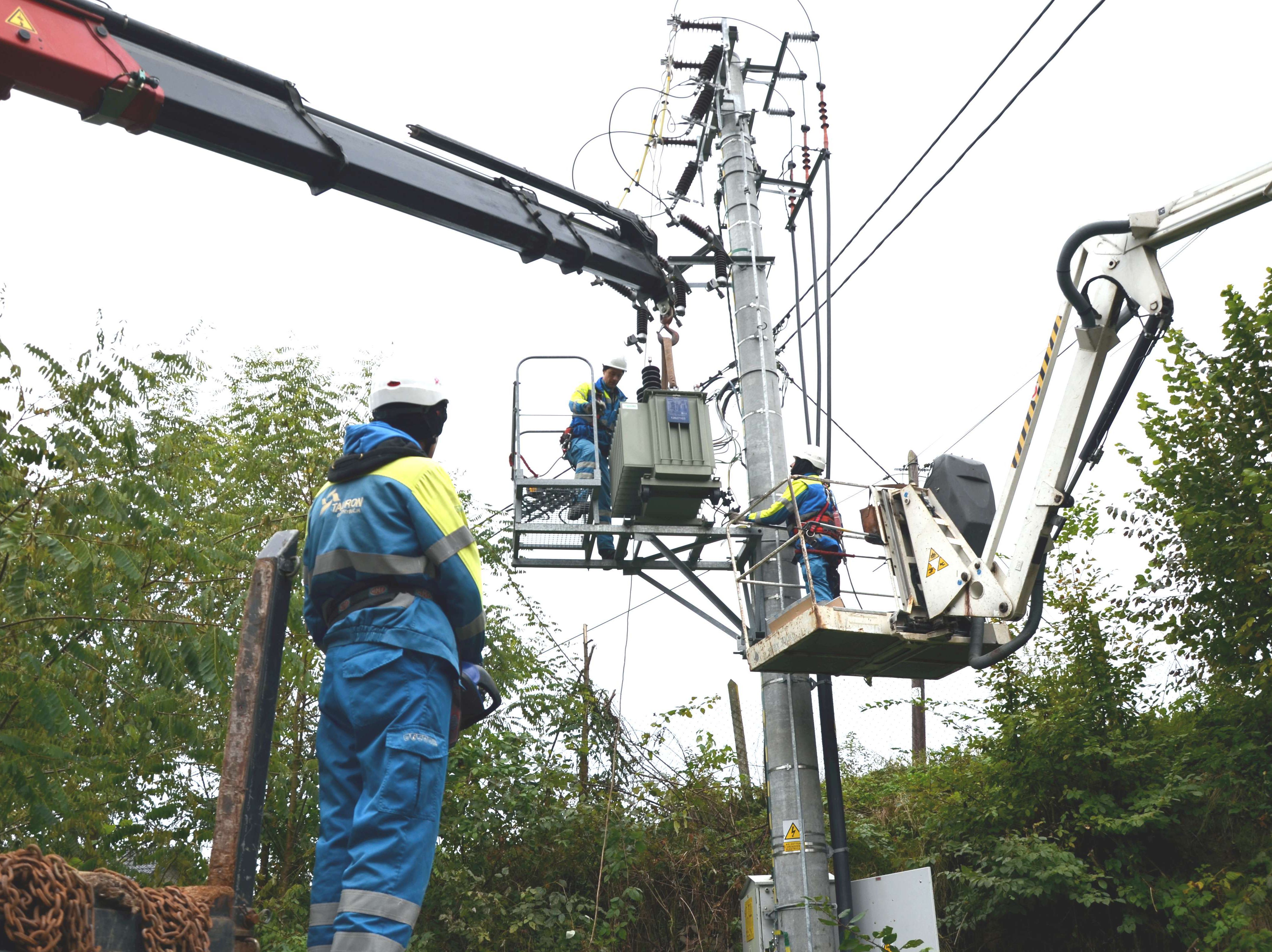 trzech elektromonterów pracuje przy montażu transformatora na słupie elektroenergetycznym