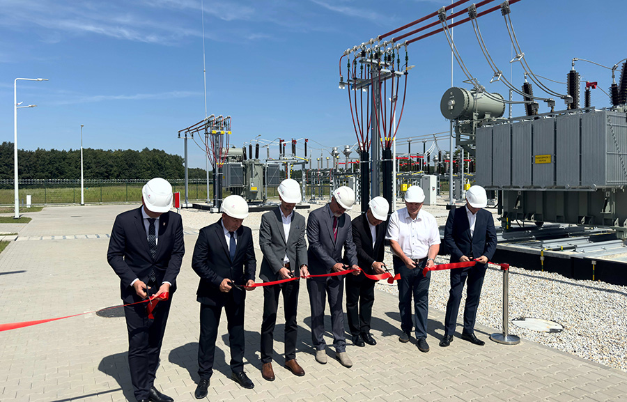 siedmiu elegancko ubranych panów przecina czerwona wstęgę na tle urządzeń stacji elektroenergetycznej