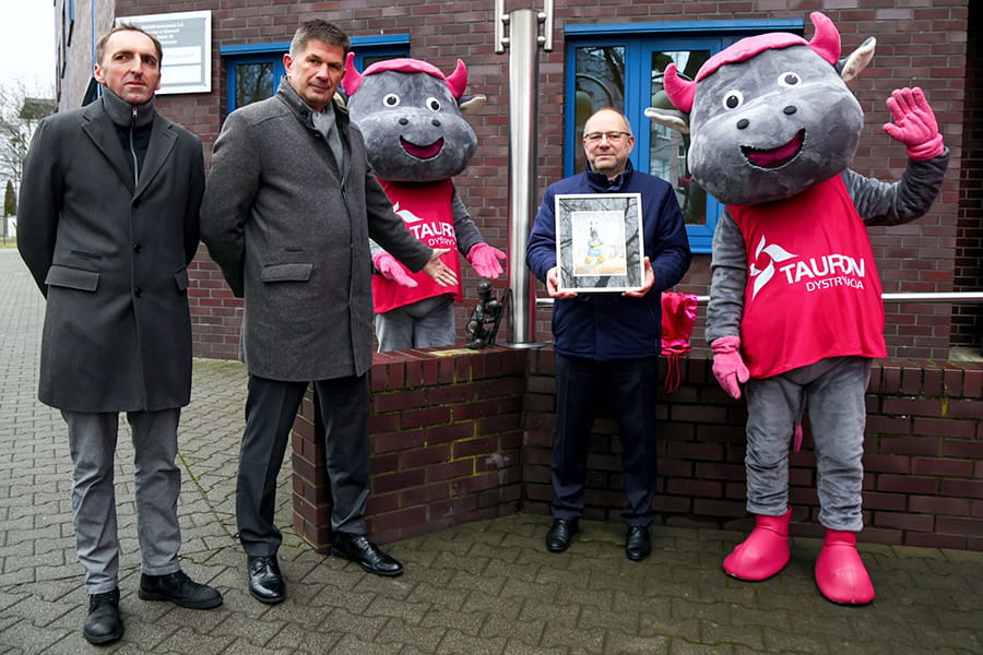 na tle budynku rejonu energetycznego w Katowicach stoi trzech panów oraz dwie maskotki - byczki Tauronki