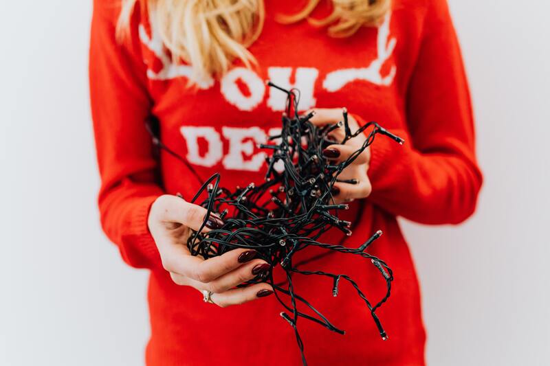 pani ubrana w czerwony sweterek trzyma w dłoniach zwinięty w kłębek łańcuszek świątecznych lampek