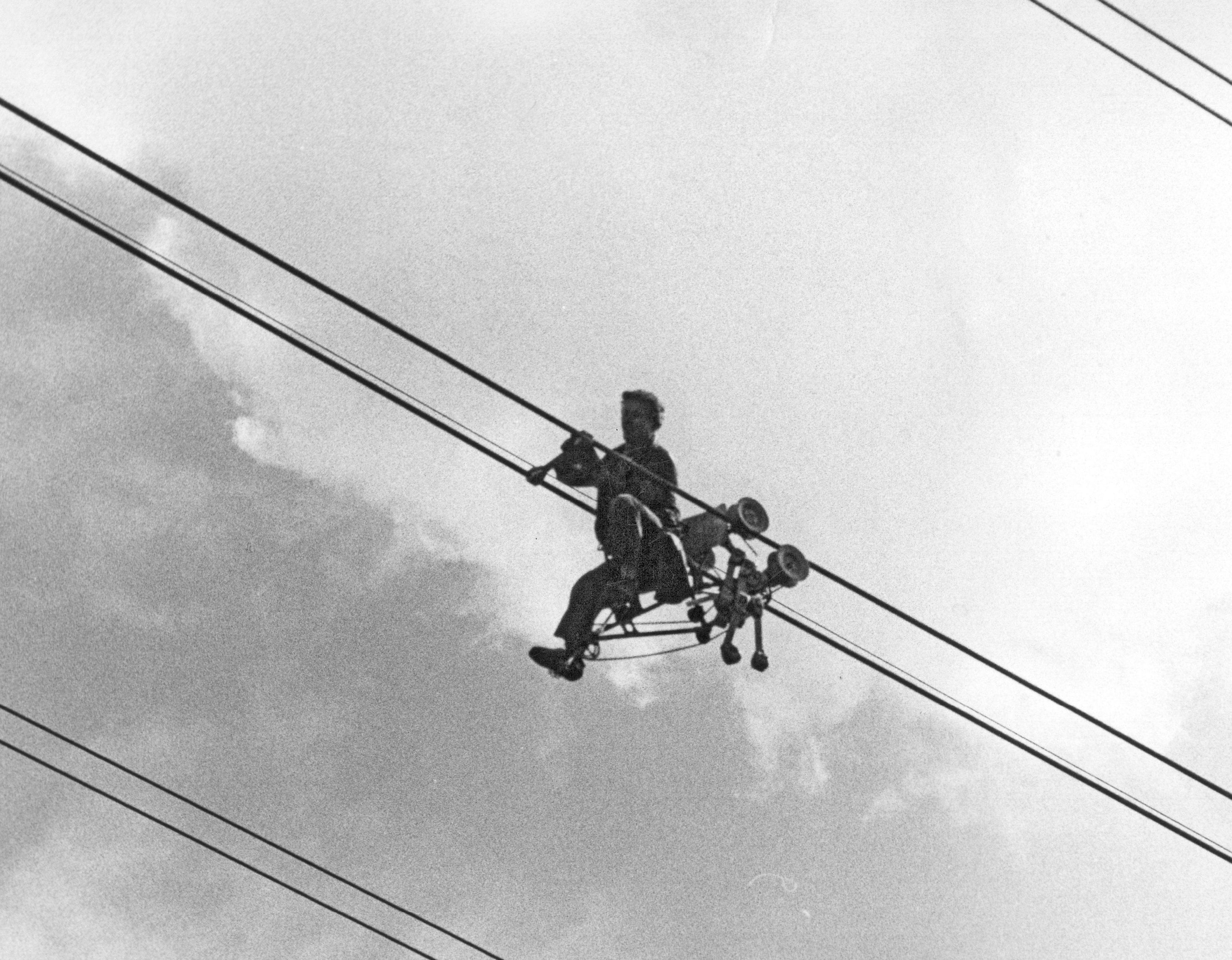 na czarnobiałym zdjęciu wykonanym w 1980 roku energetyk pracuje zawieszony w specjalnej prowadnicy na środku linii energetycznej