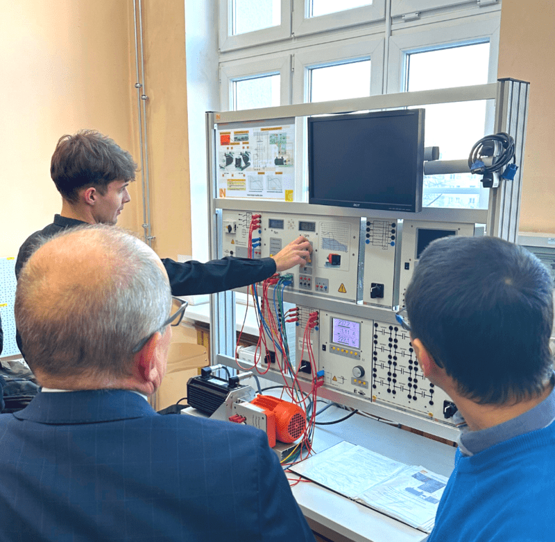 młody mężczyzna ustawia pokrętło na tablicy sterującej, czemu przygląda się dwóch panów