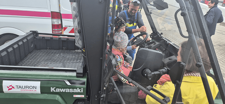 dwóch panów energetyków prezentuje dwójce dzieci samochód pogotowia energetycznego