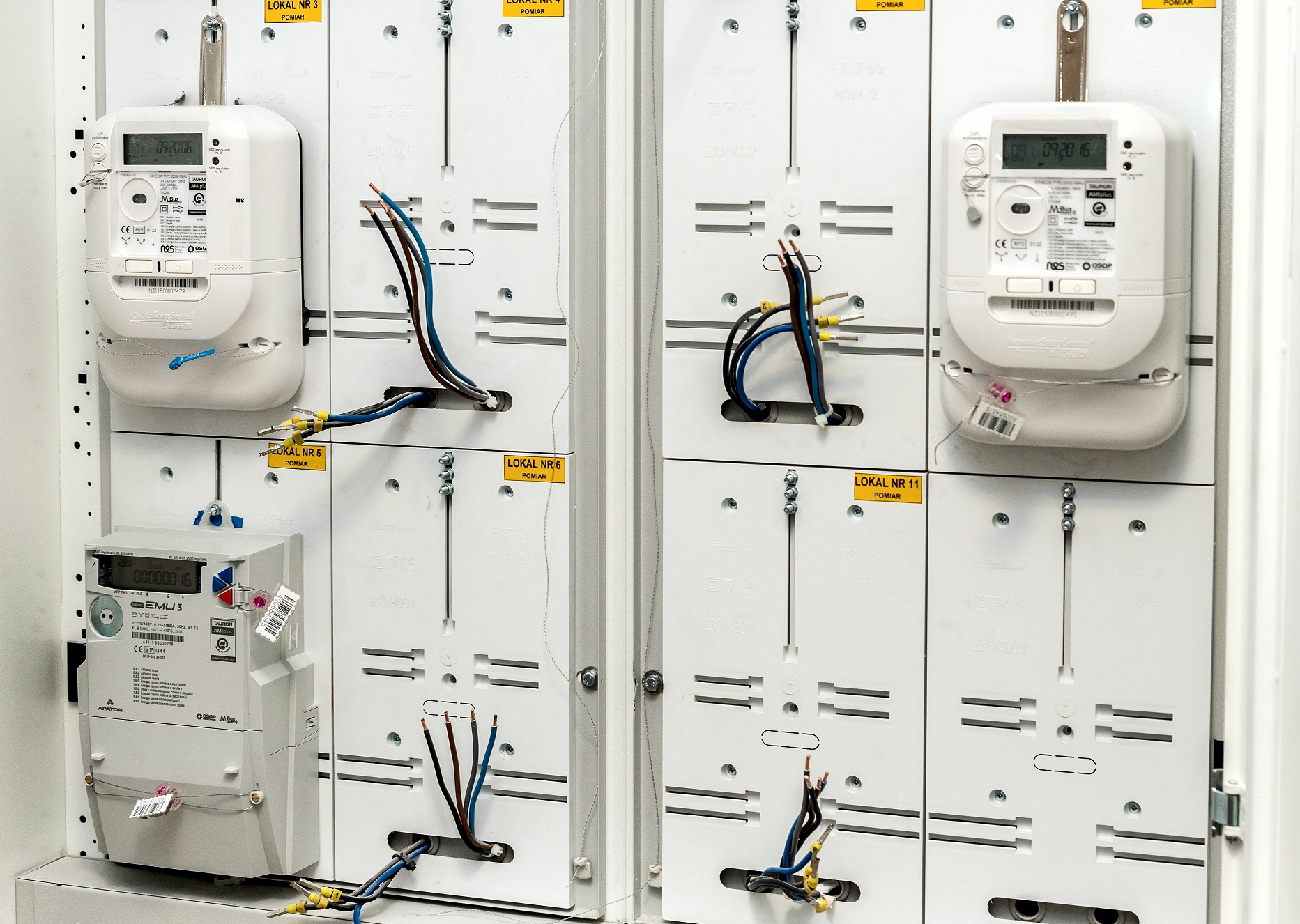 trzy białe liczniki energii elektrycznej umieszczone w szafce licznikowej domu wielorodzinnego