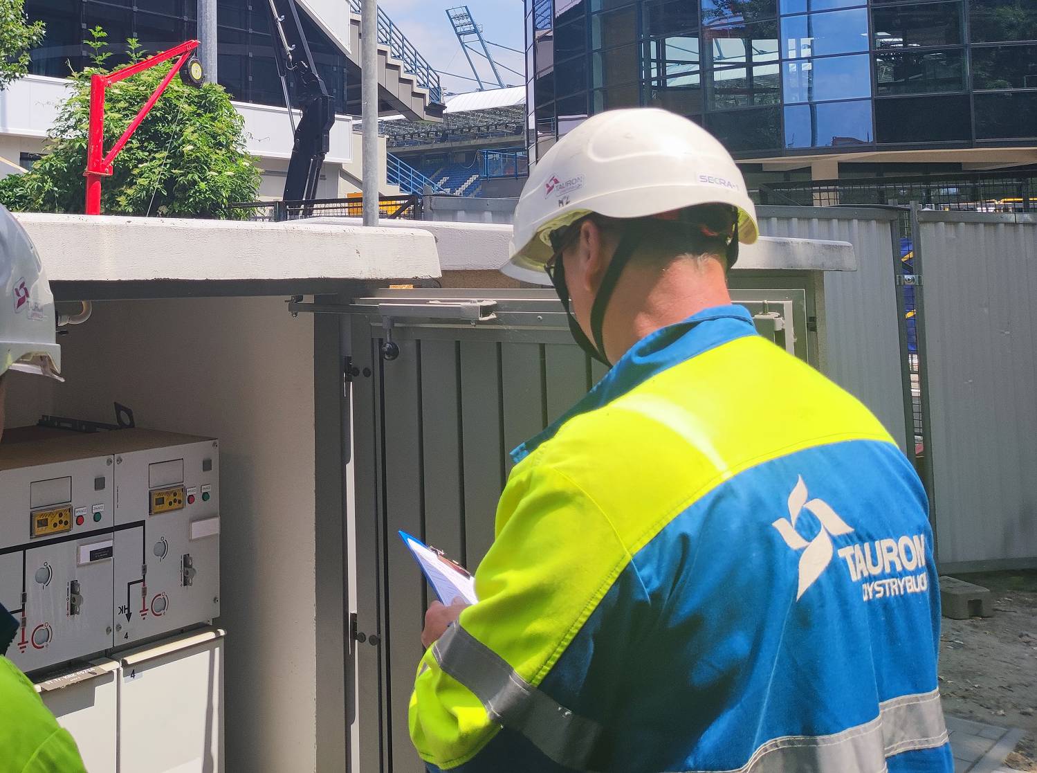 elektromonter Tauron Dystrybucja sprawdza skrzynki elektryczne pod stadionem sportowym