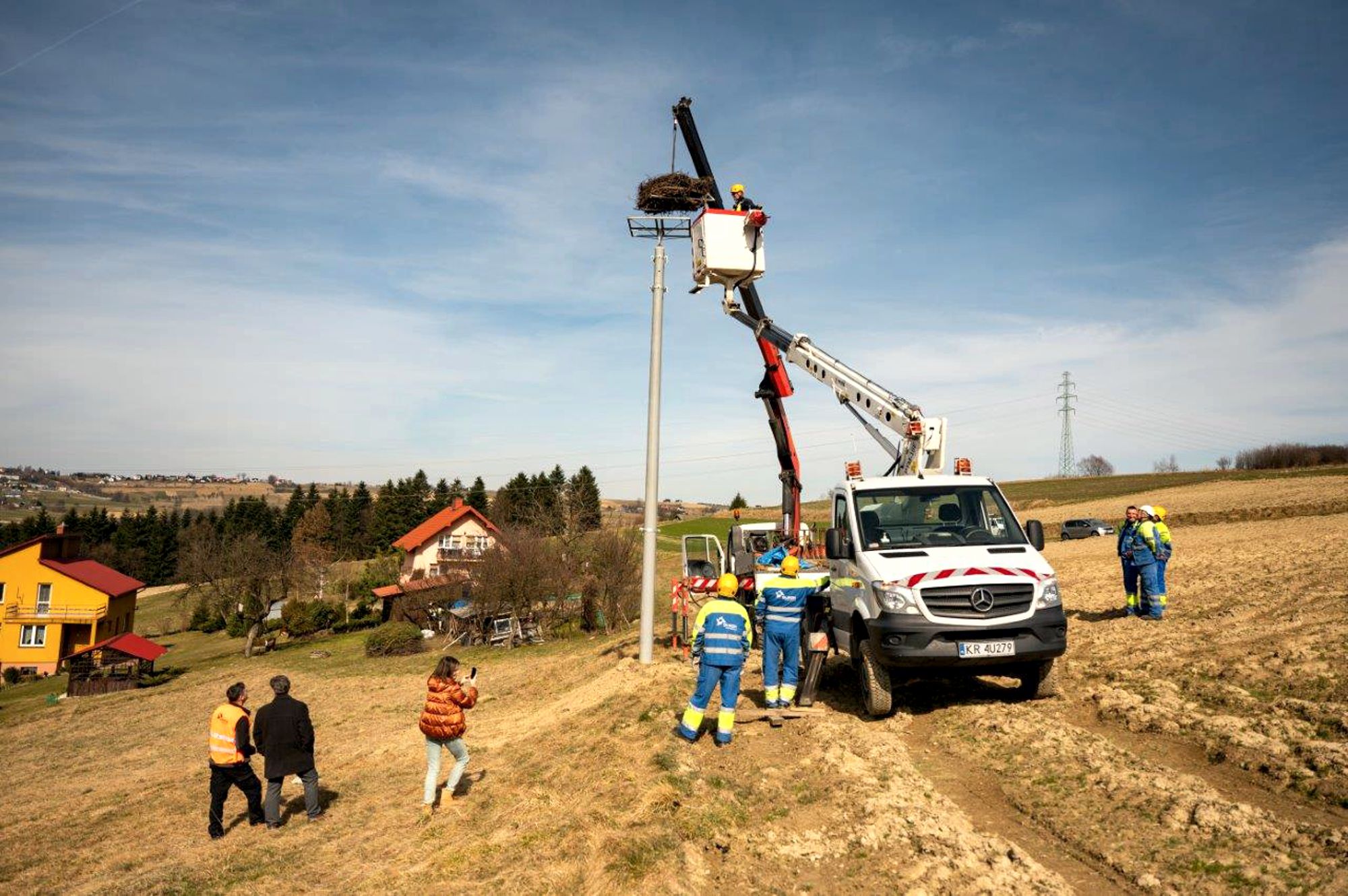 elektromonter znajdujący się w koszu podnośnika montuje bocianie gniazdo na wysokim słupie