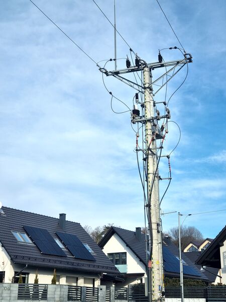 szary słup energetyczny na tle błękitnego nieba i dwóch domów jednorodzinnych