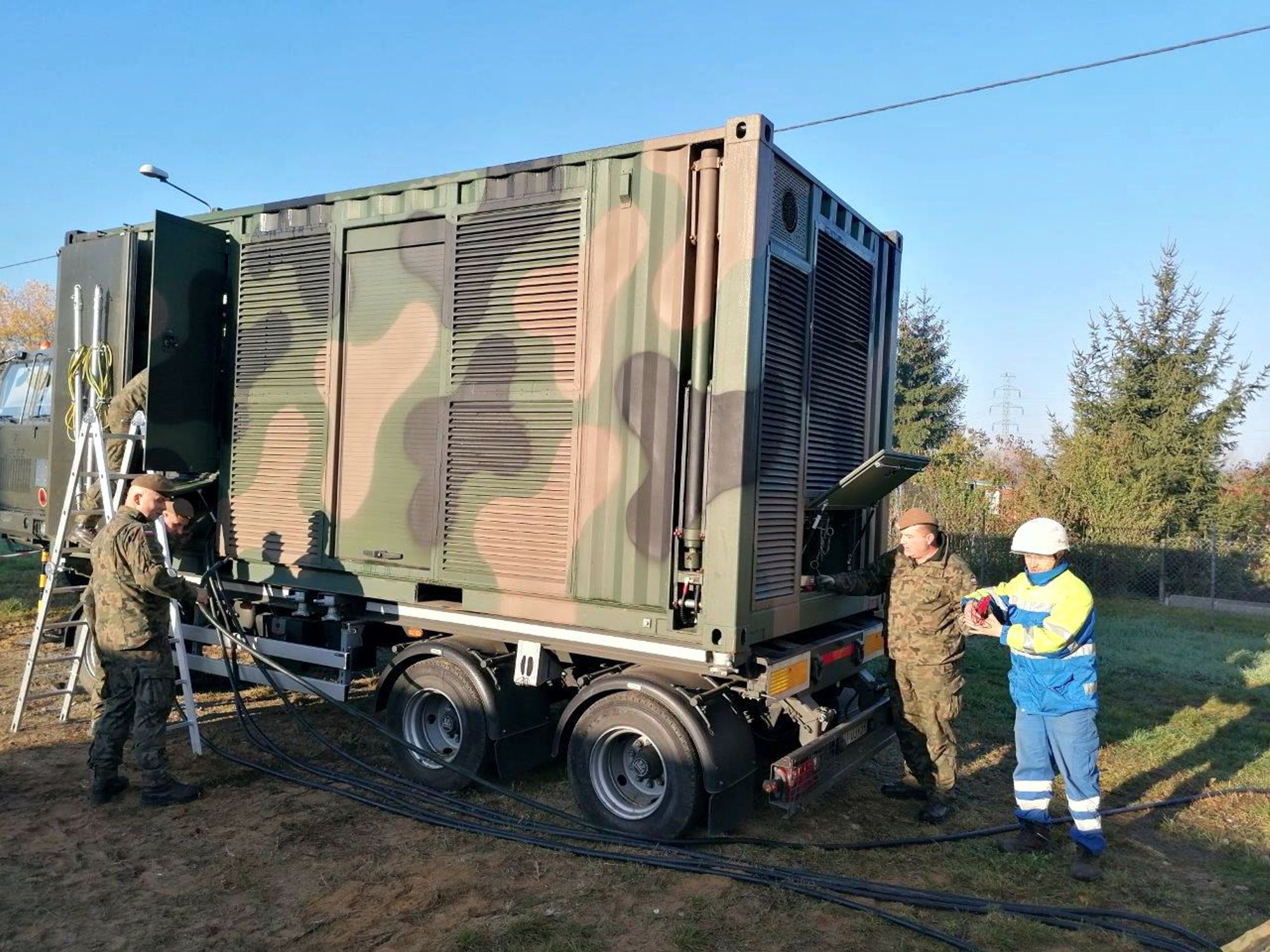 grupa żołnierzy i pracownik Tauron Dystrybucji stoją przy mobilnym magazynie energii pomalowanym w barwy ochronne