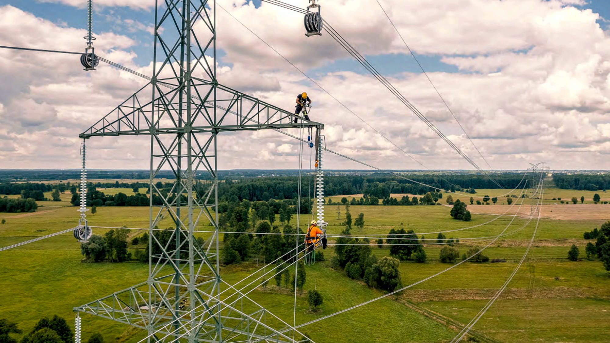 dwóch pracowników energetyki wymienia izolatory na linii energetycznej wysokiego napięcia