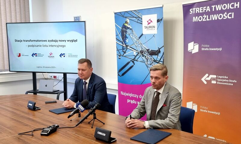 przy brązowym stoliku na tle banerów firmowych prezes TAURON Dystrybucja i prezes Legnickiej Specjalnej Strefy Ekonomicznej podpisują porozumienie