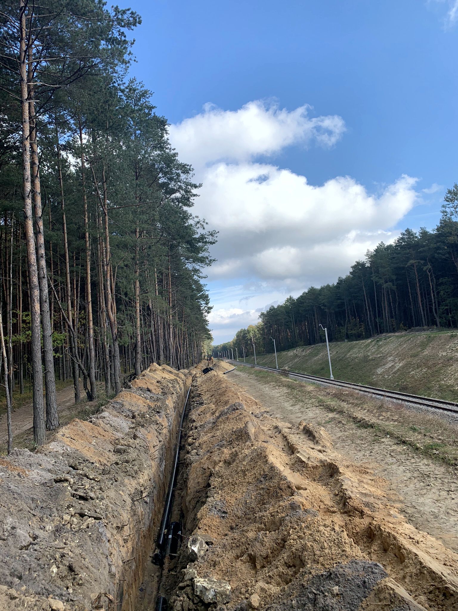 wykopany rów z umieszczonym w nim kablem energetycznym, znajdujący się przy torach kolejowych w środku lasu