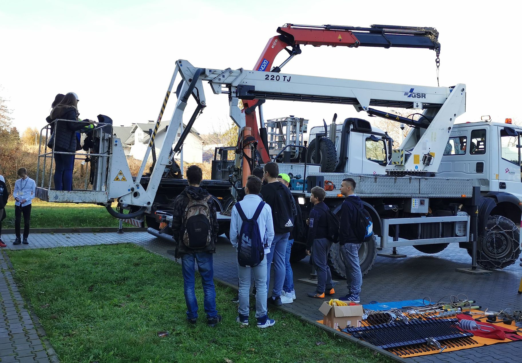 grupa uczniów znajduję się przed samochodem z zamontowanym podnośnikiem do prac na wysokości