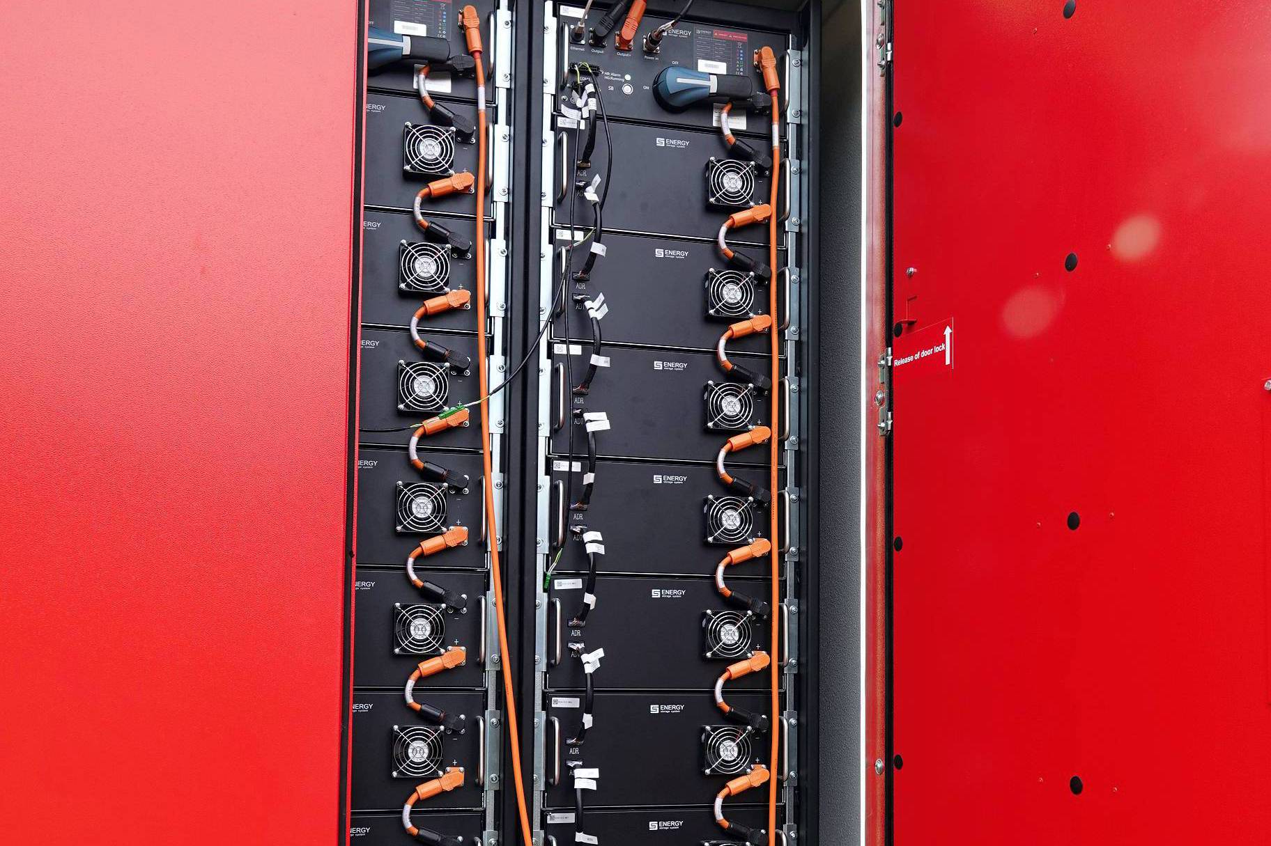 Przez otwarte drzwi magazynu energii widać osiem dużych baterii