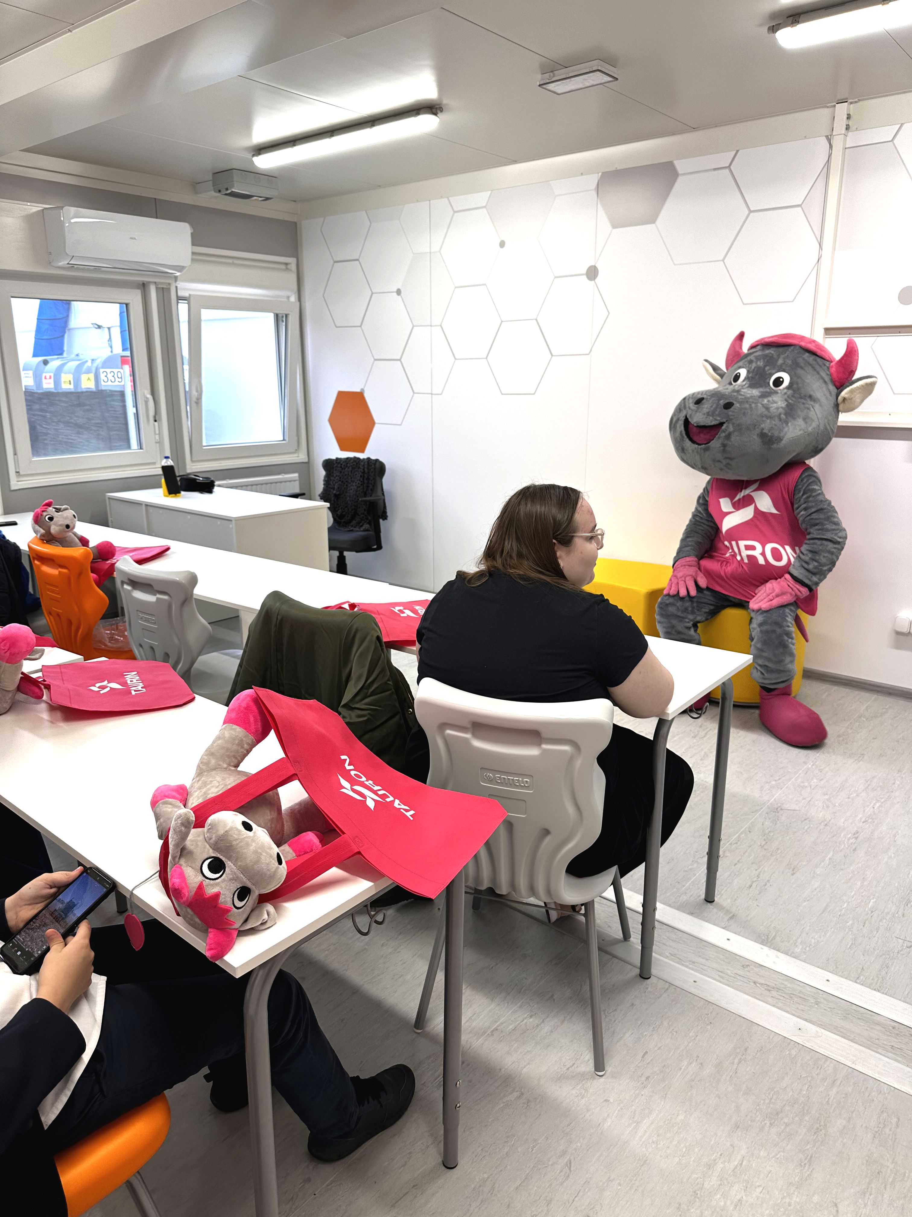 we wnętrzu klasy szkolnej w ławce siedzi dziewczynka, na którą spogląda Tauronek – maskotka w kształcie byczka 